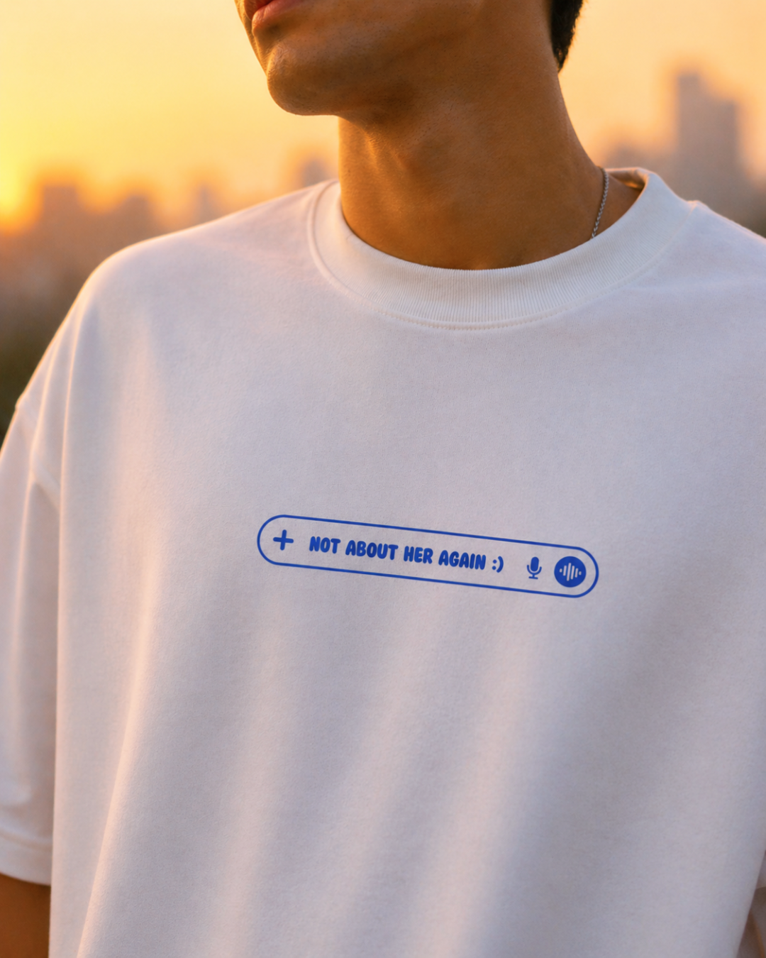 Close up shot of a person wearing a white t-shirt with a blue graphic and text "Not about her again" at sunset.