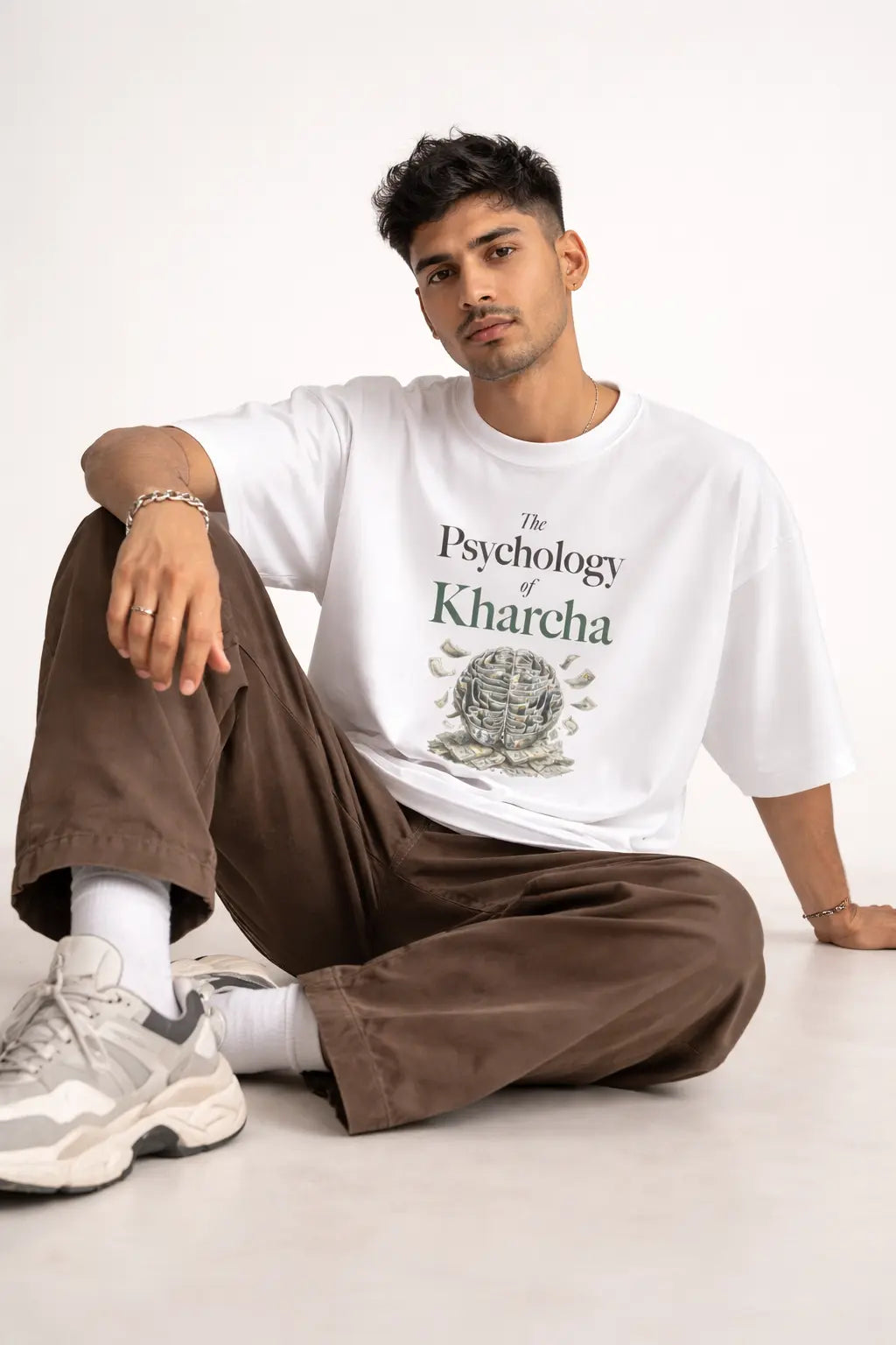 Person wearing a white t-shirt with text "The Psychology of Kharcha" and graphics, sitting on a light-colored floor.
