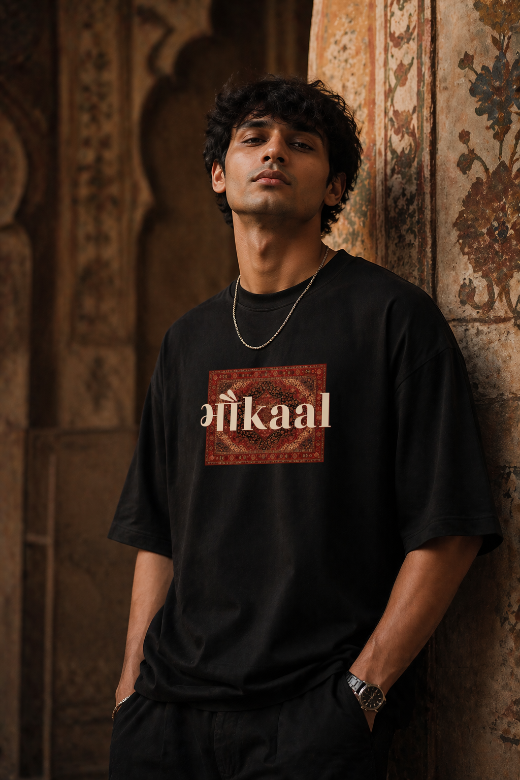 Person wearing a black t-shirt with 'bhaukaal' design against an ornate wall.