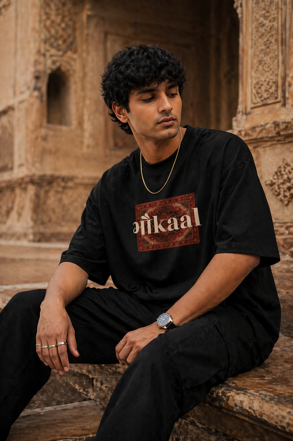 Man wearing a black t-shirt with 'Bhaukaal' logo sitting in front of an architectural background