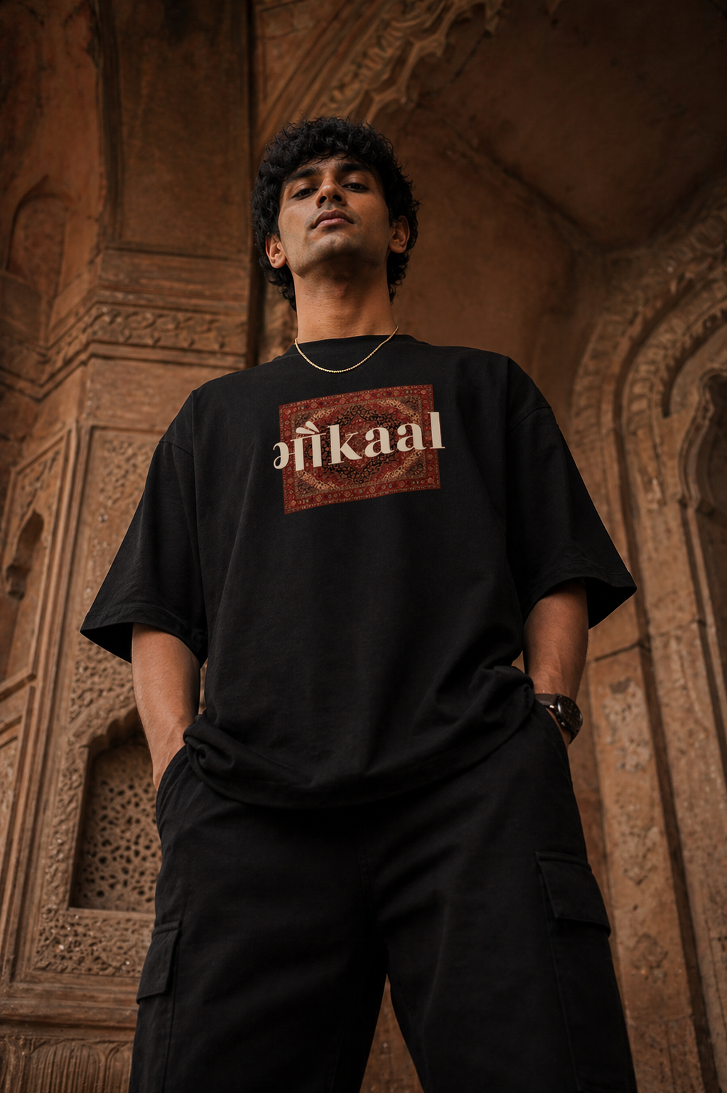 bottom shot of a person wearing a black t-shirt with 'bhaukaal' logo against an architectural background