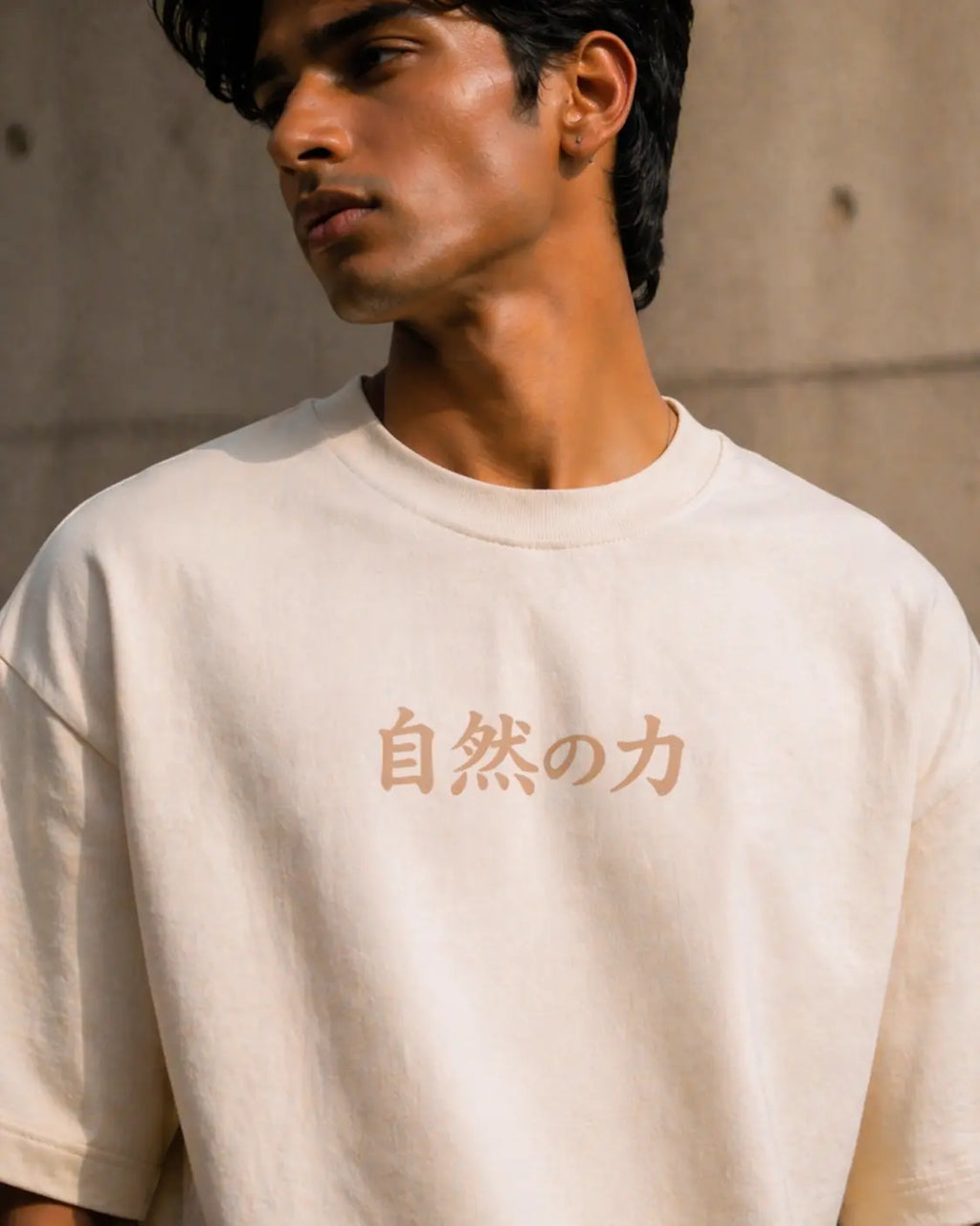 Man wearing a beige t-shirt with Japanese text against a concrete wall.