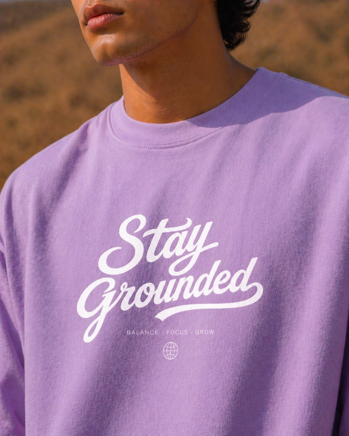 Close up shot of a person wearing a lavender oversized t-shirt with 'Stay Grounded' text